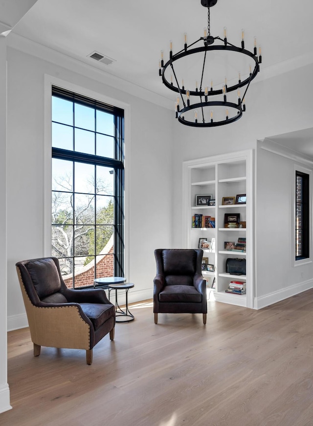 sitting room featuring built in features, visible vents, an inviting chandelier, ornamental molding, and wood finished floors