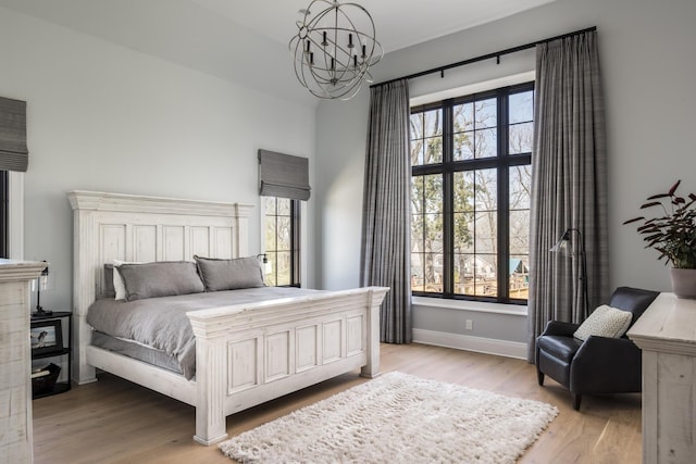 bedroom with light wood finished floors, multiple windows, baseboards, and a notable chandelier