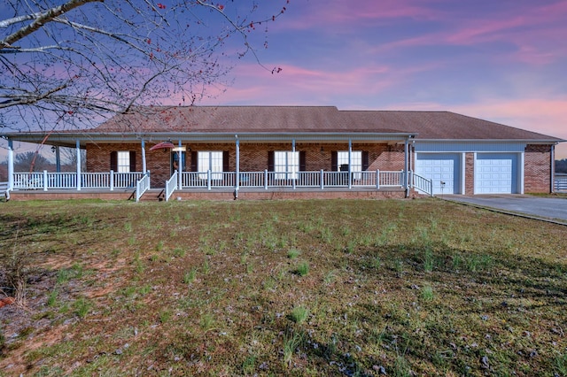 view of front of house with driveway, an attached garage, covered porch, a yard, and brick siding