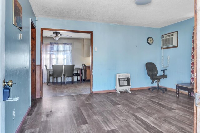 interior space with a textured ceiling, wood finished floors, a ceiling fan, a wall mounted AC, and heating unit