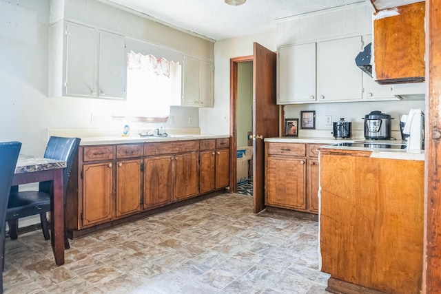 kitchen featuring brown cabinets, light countertops, a textured ceiling, under cabinet range hood, and a sink