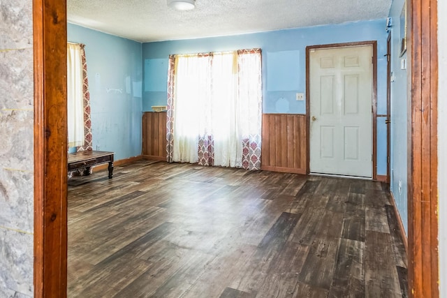 empty room with a wainscoted wall, dark wood-type flooring, a textured ceiling, and wooden walls