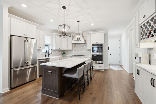 kitchen featuring white cabinets, appliances with stainless steel finishes, dark wood-type flooring, a center island, and a sink