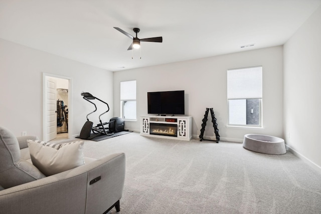 carpeted living room featuring baseboards, visible vents, a ceiling fan, and a glass covered fireplace