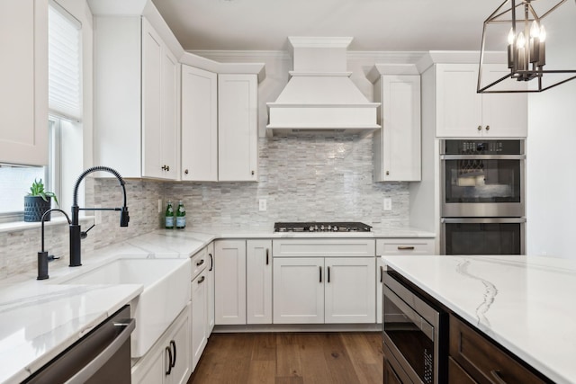 kitchen featuring white cabinets, appliances with stainless steel finishes, light stone countertops, custom exhaust hood, and backsplash