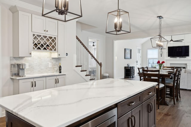 kitchen with tasteful backsplash, white cabinets, open floor plan, wood finished floors, and ceiling fan with notable chandelier