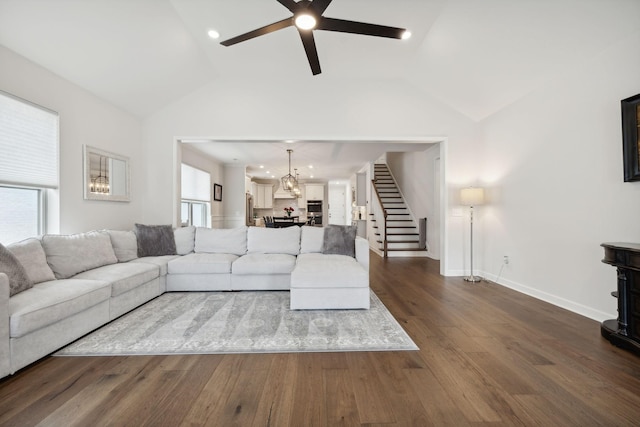 living area featuring dark wood-style flooring, lofted ceiling, ceiling fan, baseboards, and stairs