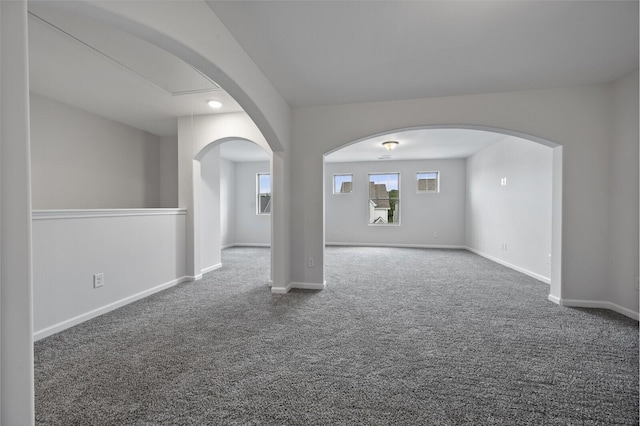 unfurnished room featuring carpet floors, arched walkways, and baseboards