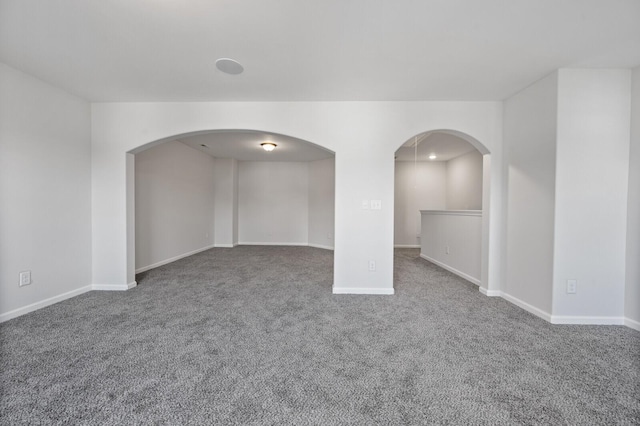 empty room featuring carpet, arched walkways, and baseboards