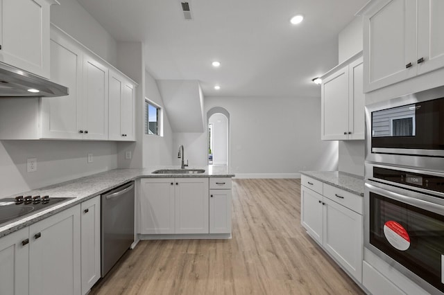 kitchen featuring arched walkways, appliances with stainless steel finishes, a sink, light wood-type flooring, and a peninsula