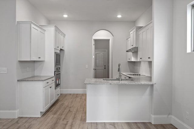 kitchen with light wood finished floors, white cabinets, a sink, a peninsula, and under cabinet range hood