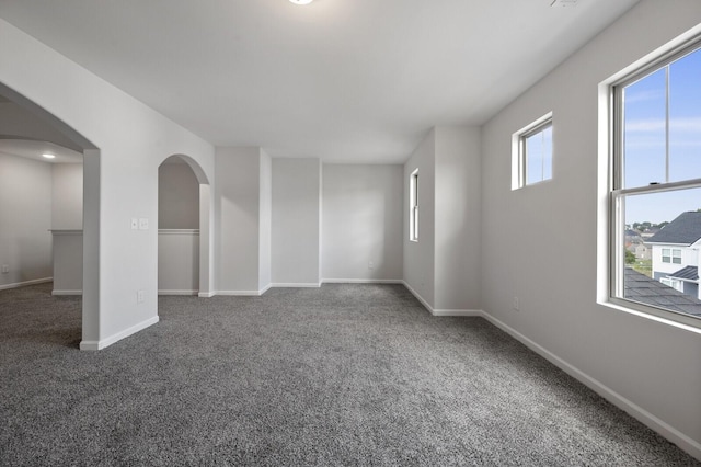 carpeted empty room featuring arched walkways and baseboards