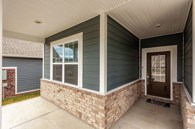 view of exterior entry with a porch and brick siding