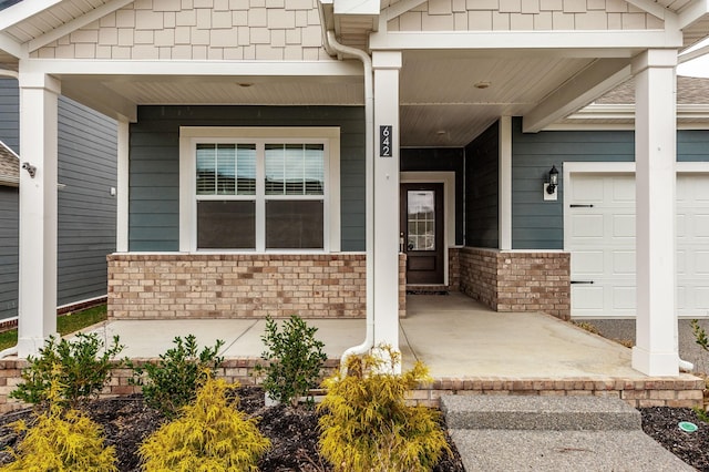 view of exterior entry with brick siding, covered porch, and an attached garage