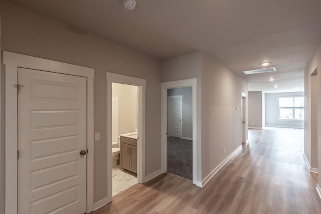 hall with visible vents, baseboards, and light wood-style floors