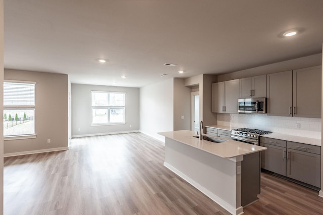 kitchen featuring light wood finished floors, a sink, appliances with stainless steel finishes, light countertops, and decorative backsplash