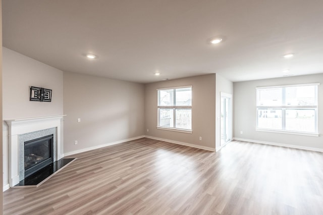 unfurnished living room with a glass covered fireplace, recessed lighting, baseboards, and wood finished floors