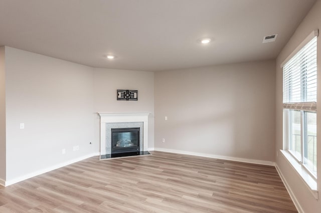 unfurnished living room featuring a fireplace with flush hearth, visible vents, baseboards, and light wood-style floors