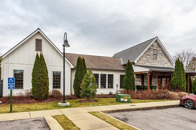 view of front of home featuring a standing seam roof, stone siding, roof with shingles, board and batten siding, and metal roof