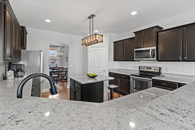 kitchen with arched walkways, light stone counters, wood finished floors, stainless steel appliances, and dark brown cabinets