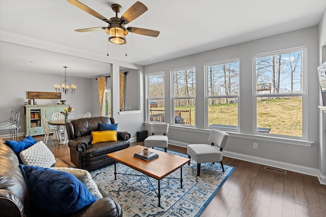 living area featuring ceiling fan with notable chandelier, wood finished floors, visible vents, and baseboards