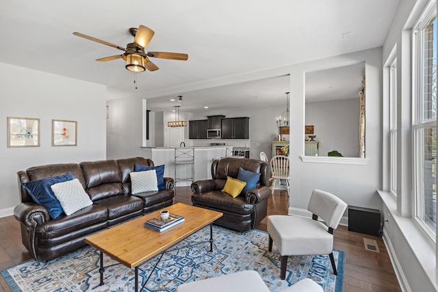 living room with ceiling fan with notable chandelier, hardwood / wood-style floors, visible vents, and baseboards