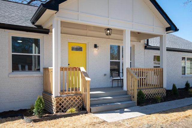 property entrance with covered porch, brick siding, and roof with shingles