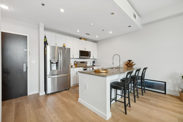 kitchen featuring stainless steel appliances, light wood-type flooring, a sink, and a kitchen bar