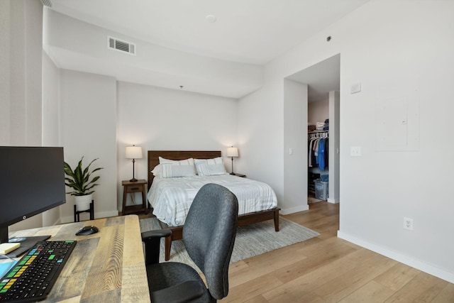 bedroom with visible vents, a spacious closet, light wood-type flooring, electric panel, and baseboards