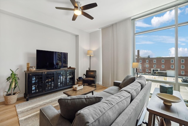 living area with a wall of windows, ceiling fan, baseboards, and wood finished floors