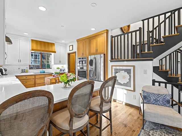 kitchen with stainless steel appliances, a sink, light countertops, light wood-type flooring, and backsplash