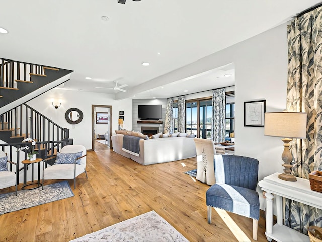 living room with a ceiling fan, wood-type flooring, a fireplace, and stairs