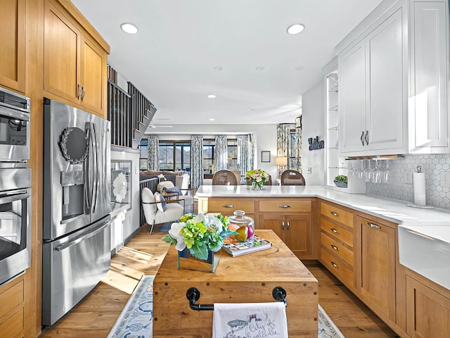 kitchen featuring a peninsula, open floor plan, light wood-type flooring, stainless steel fridge with ice dispenser, and tasteful backsplash