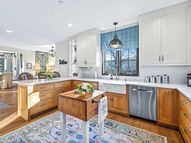 kitchen with a peninsula, wood finished floors, a sink, light countertops, and stainless steel dishwasher