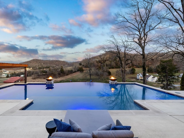 pool at dusk with an infinity pool and a patio area