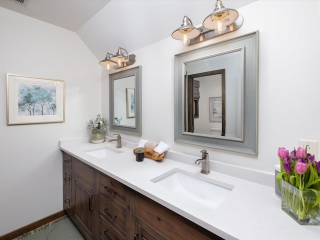 bathroom featuring double vanity, baseboards, vaulted ceiling, and a sink