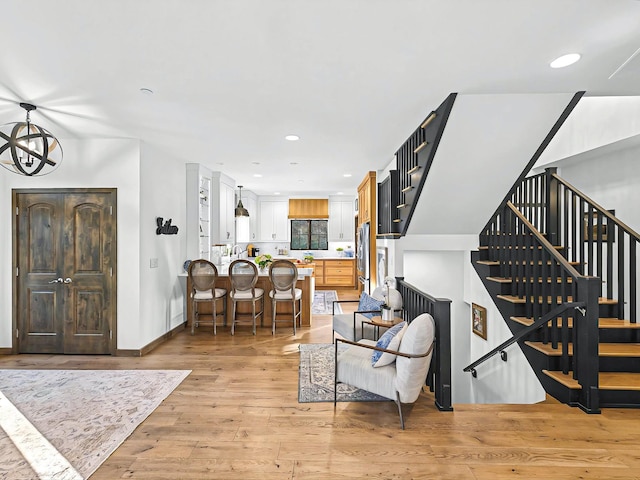 living area with recessed lighting, light wood-style flooring, a chandelier, baseboards, and stairs