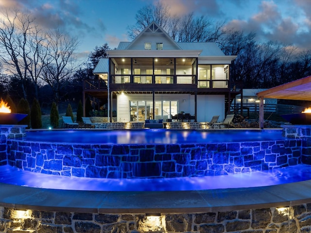 back of property at dusk featuring an infinity pool, metal roof, stairs, and a sunroom