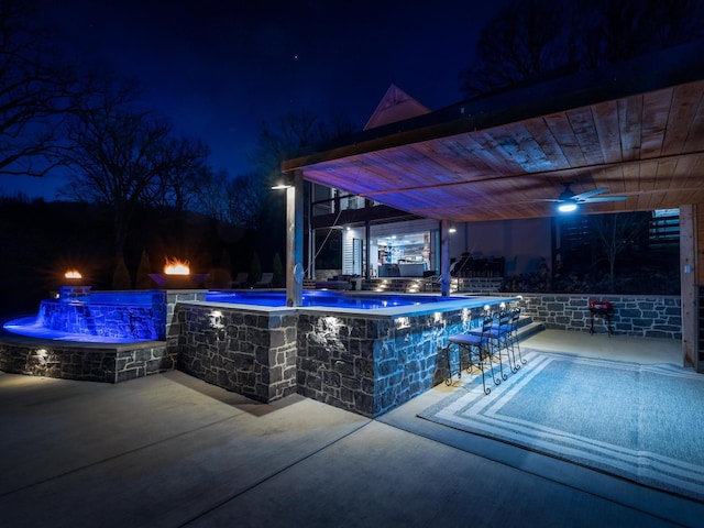 pool at night with outdoor dry bar, a patio, and a ceiling fan