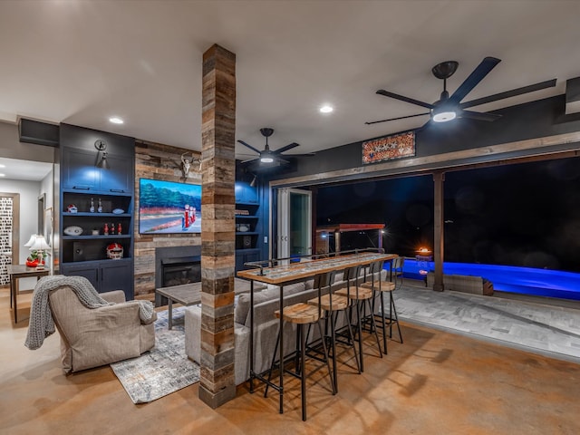 bar featuring concrete flooring, recessed lighting, a fireplace, a ceiling fan, and ornate columns