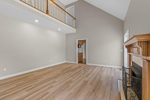 unfurnished living room with high vaulted ceiling, recessed lighting, a fireplace, baseboards, and light wood finished floors