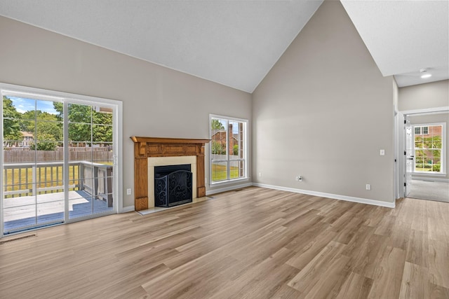 unfurnished living room featuring high vaulted ceiling, light wood-style flooring, a fireplace with flush hearth, visible vents, and baseboards