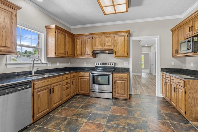 kitchen featuring stainless steel appliances, brown cabinetry, ornamental molding, a sink, and under cabinet range hood