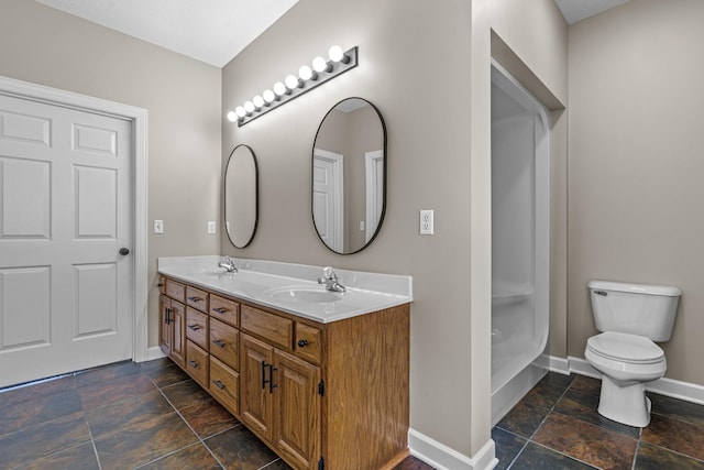 bathroom with toilet, stone finish flooring, baseboards, and a sink