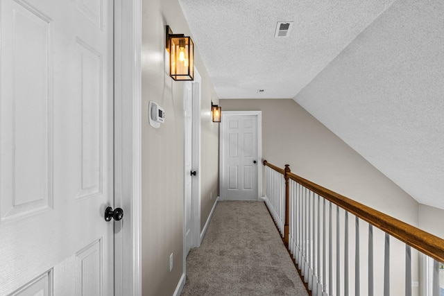 hall featuring a textured ceiling, carpet flooring, visible vents, and lofted ceiling