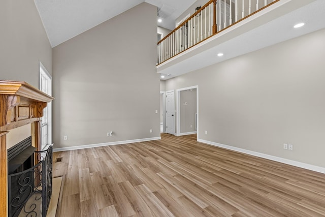 unfurnished living room with baseboards, light wood-type flooring, a fireplace, high vaulted ceiling, and recessed lighting