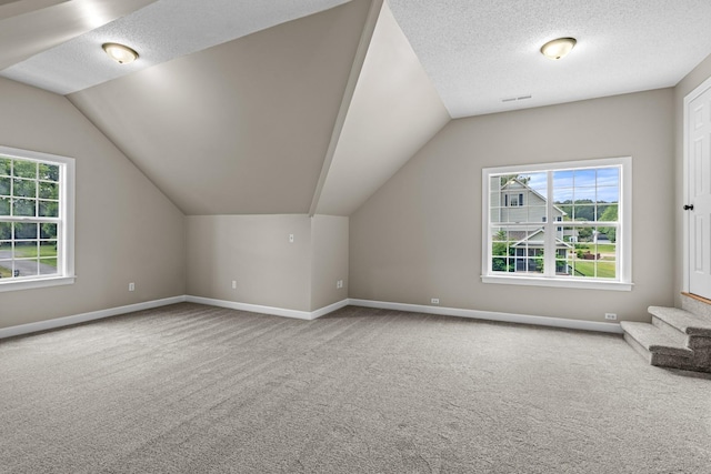 bonus room featuring a textured ceiling, carpet floors, vaulted ceiling, and baseboards