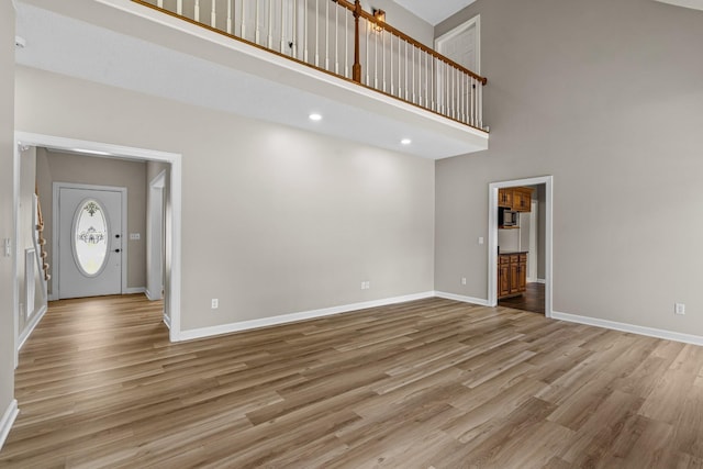 unfurnished living room with wood finished floors, a towering ceiling, and baseboards