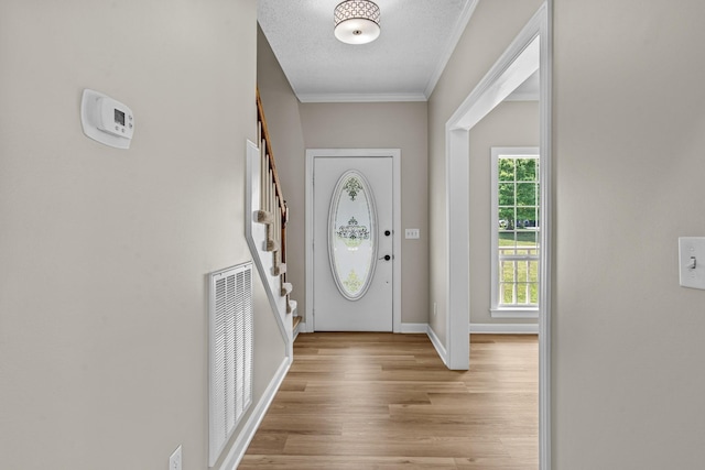 foyer entrance with visible vents, baseboards, stairs, light wood-style floors, and ornamental molding