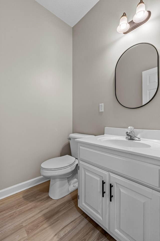 half bath with vanity, wood finished floors, toilet, and baseboards